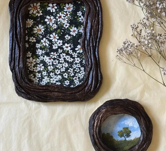 Two hand-built ceramic frames with white blossom and a small round landscape