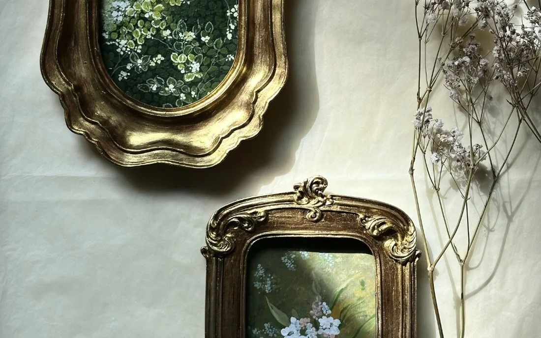 Antique gilded frames, one holding a painting of white blossom on dark green