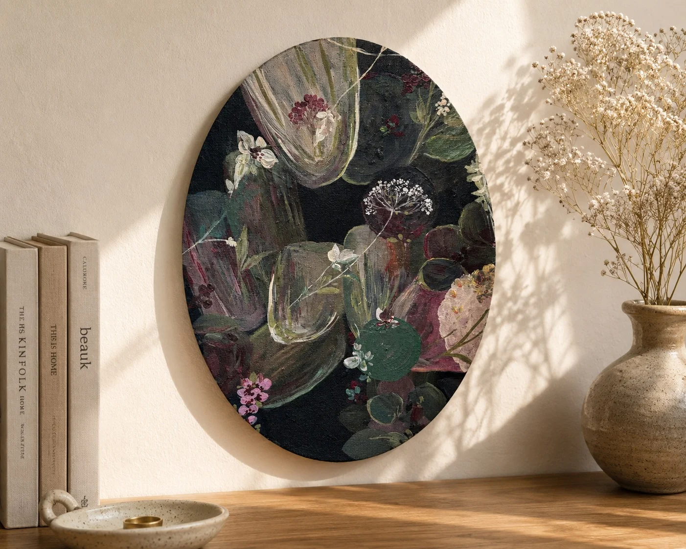 An oval painting of blossom on a dark ground standing on a shelf