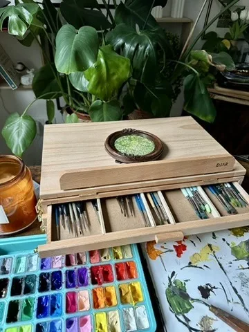A wooden paint box with gouache pans and a round ceramic frame