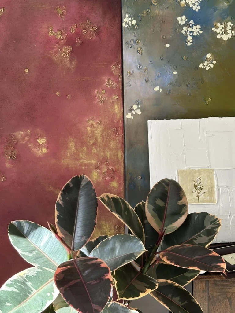 Large textured paintings on the studio wall, houseplants in front